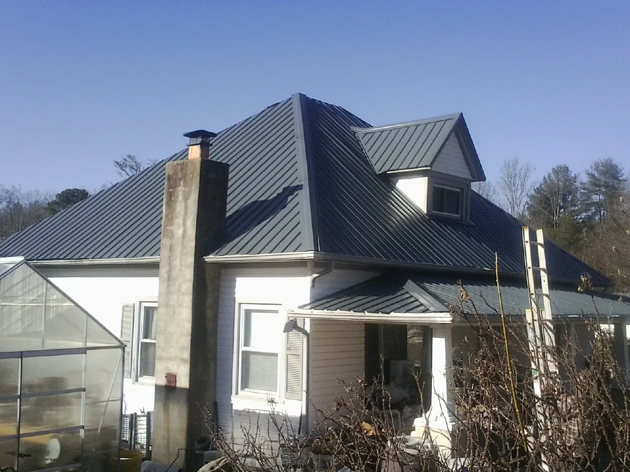 Dark blue standing seam metal roof on a white farmhouse with dormer — Slate & Tile Roof Repair by Roofing Brothers in Crested Butte