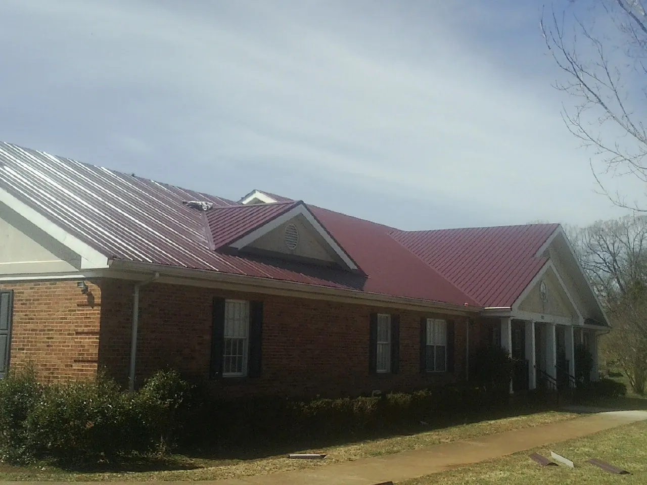 Red metal roof with gabled entries on a long brick building, from a Hail Damage Roof Repair job in Crested Butte