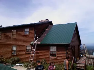 Green metal roof going on a two story log home with ladders set in Crested Butte