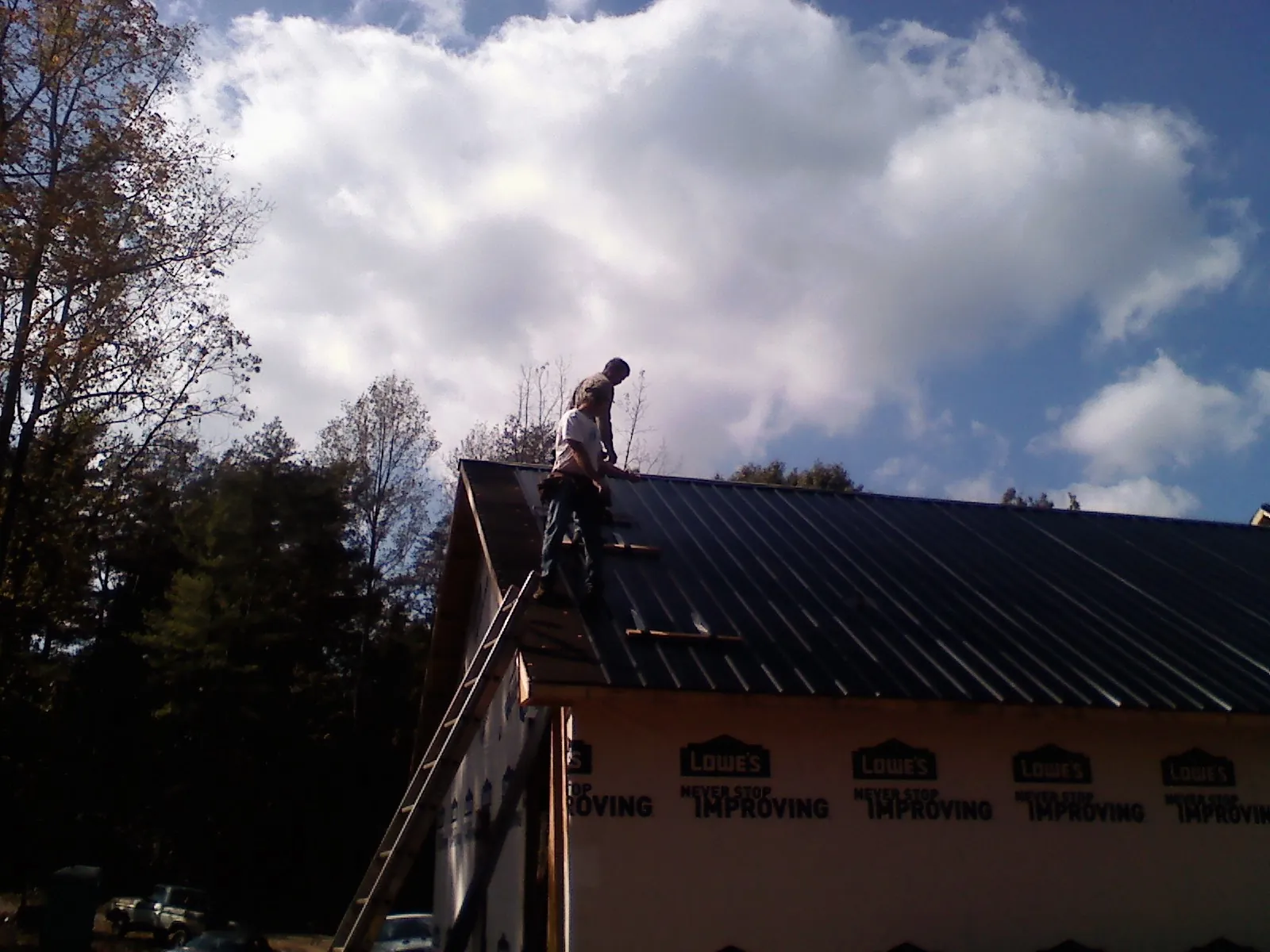 Roofer fastening dark metal panels high against a cloudy sky, from a Roof Inspection job in Crested Butte
